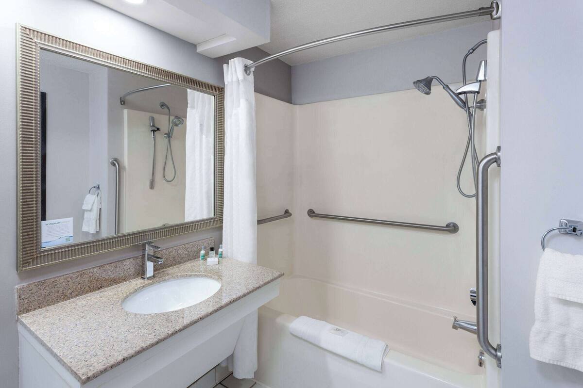 A bathroom with a sink, mirror, shower, and grab bars.