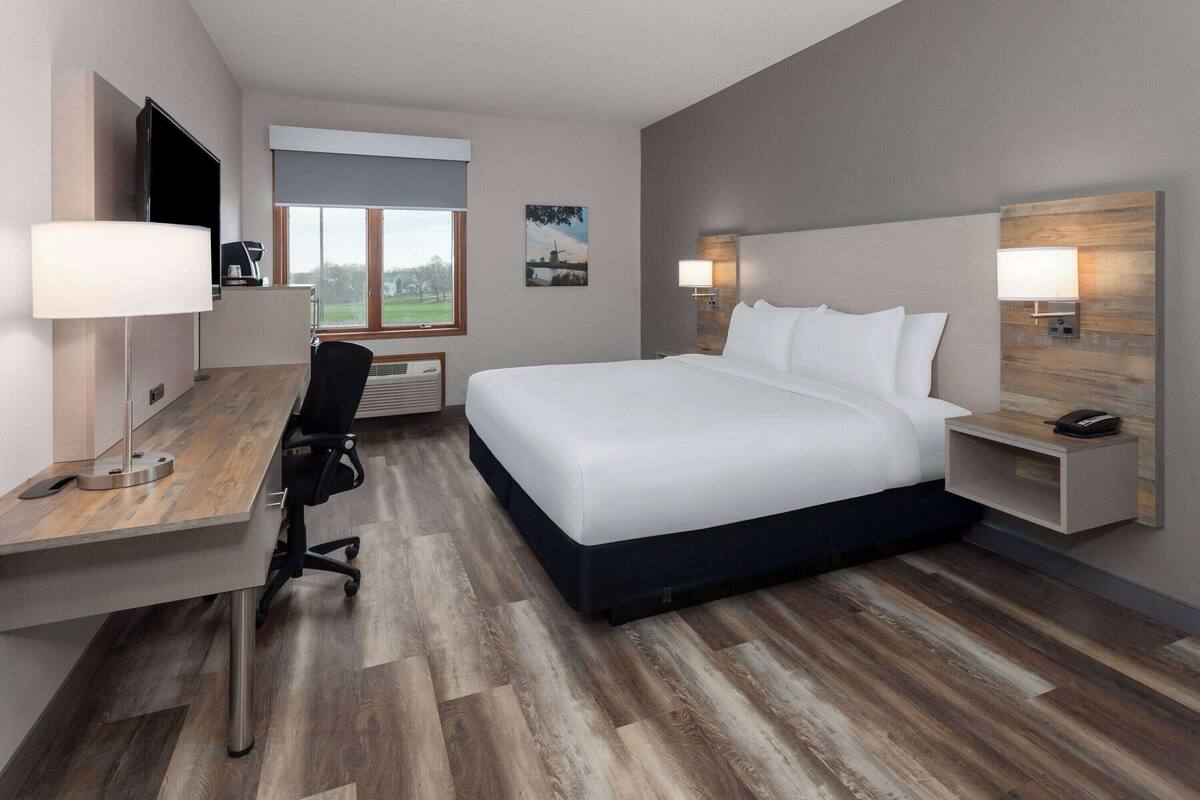 A modern hotel room with a large bed, a desk, and a TV.