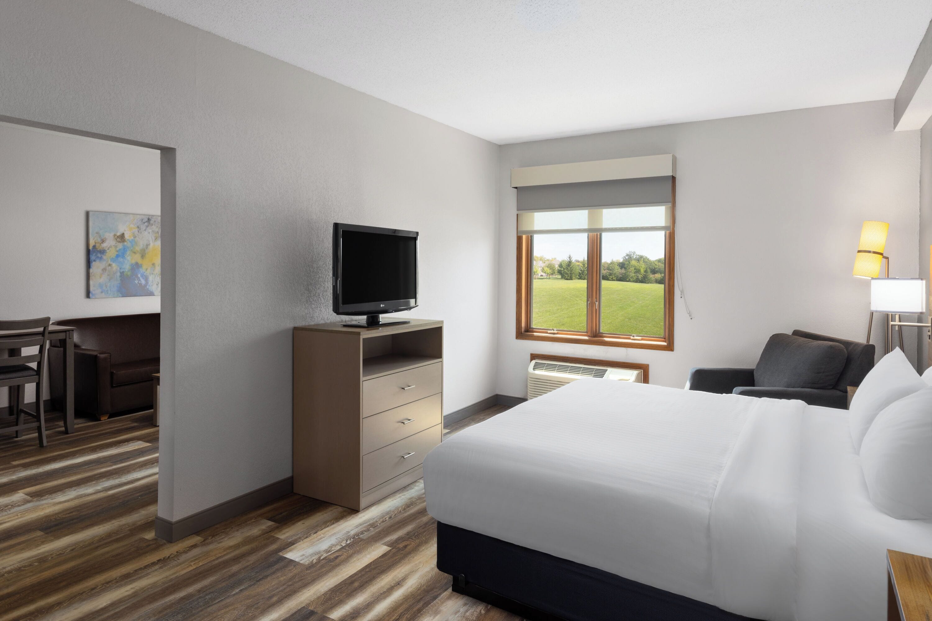 A hotel room with a bed, a desk, a television, a window with a view of the outdoors, and a lamp.