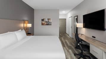 Una habitación de hotel con cama, escritorio, silla, televisor y una obra de arte en la pared.