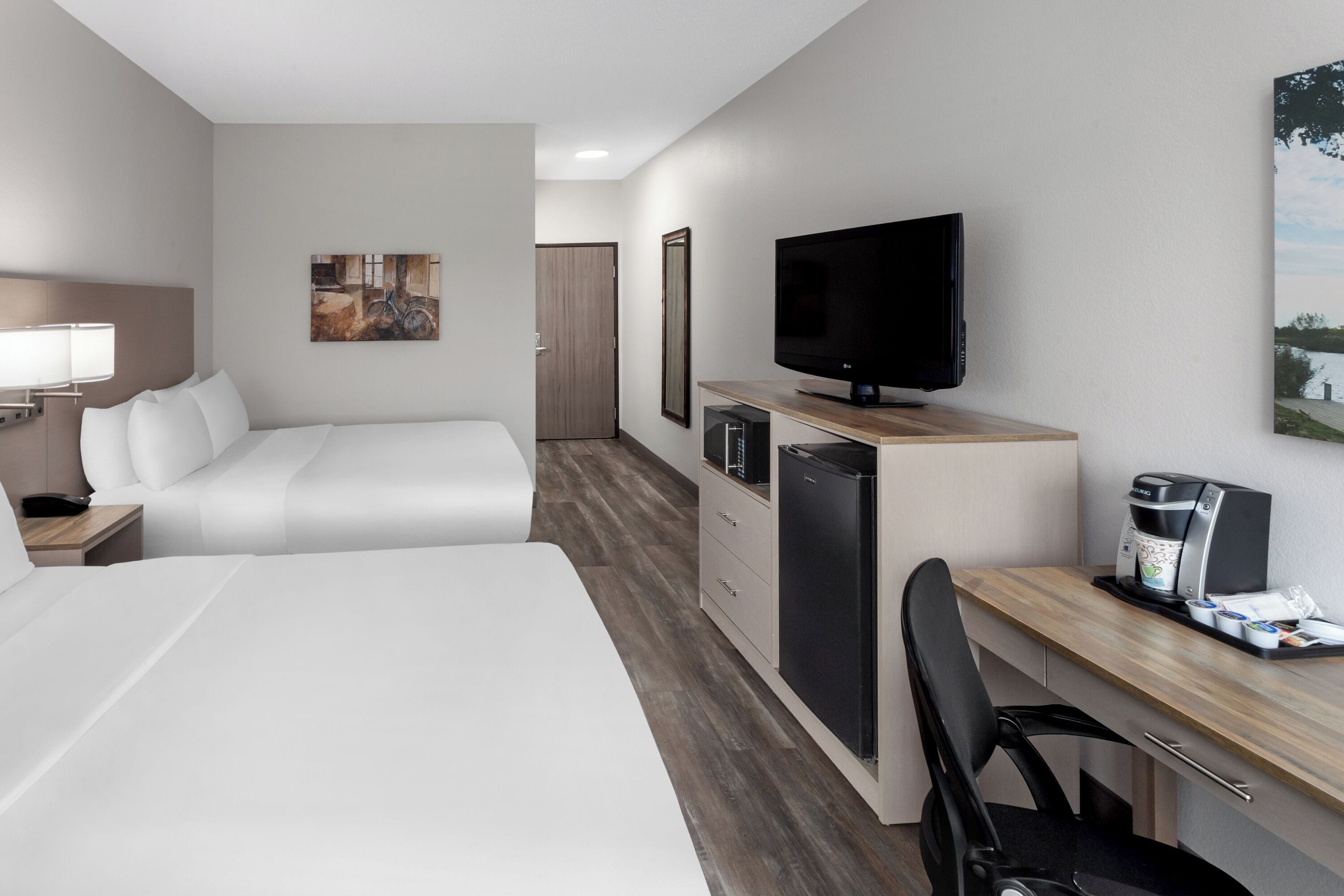 A hotel room with two beds, a desk with a coffee maker, a TV, and a refrigerator.