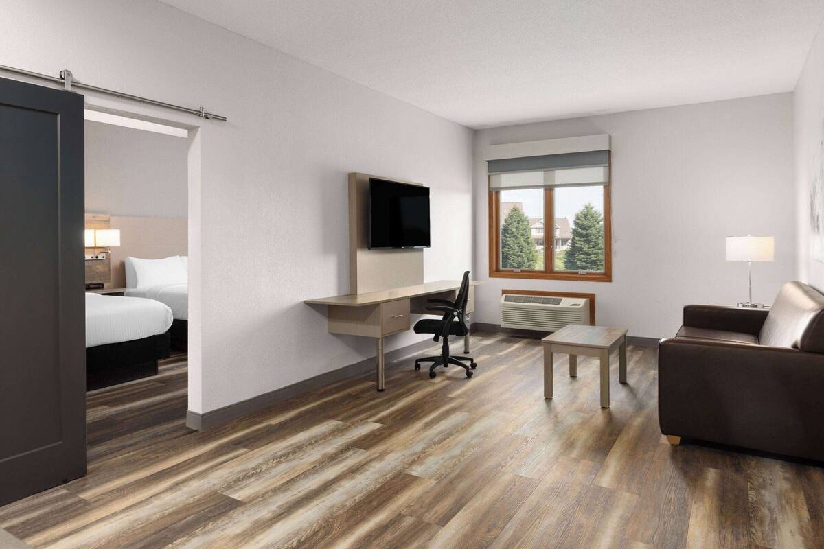 A hotel room with a bed, desk, chair, TV, and a window with a view of trees.