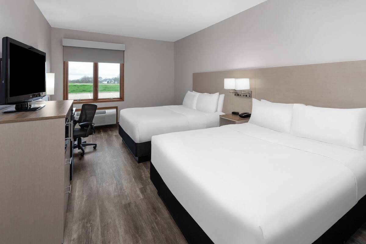 A hotel room with two beds, a desk with a computer, a TV, and a window with a view of the outdoors.