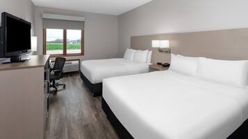 Habitación de hotel con dos camas, un escritorio con ordenador, televisor y ventana con vistas al exterior.