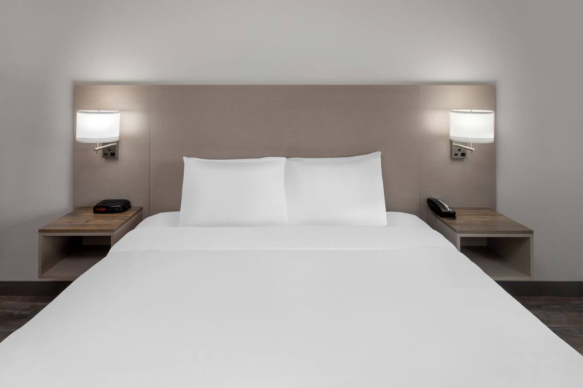A modern hotel room with a large bed, two bedside tables, and wall-mounted lamps.