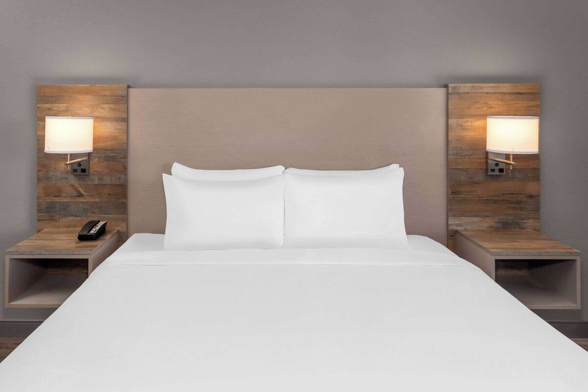 A hotel room with a large bed, two bedside tables, and wall-mounted lamps.