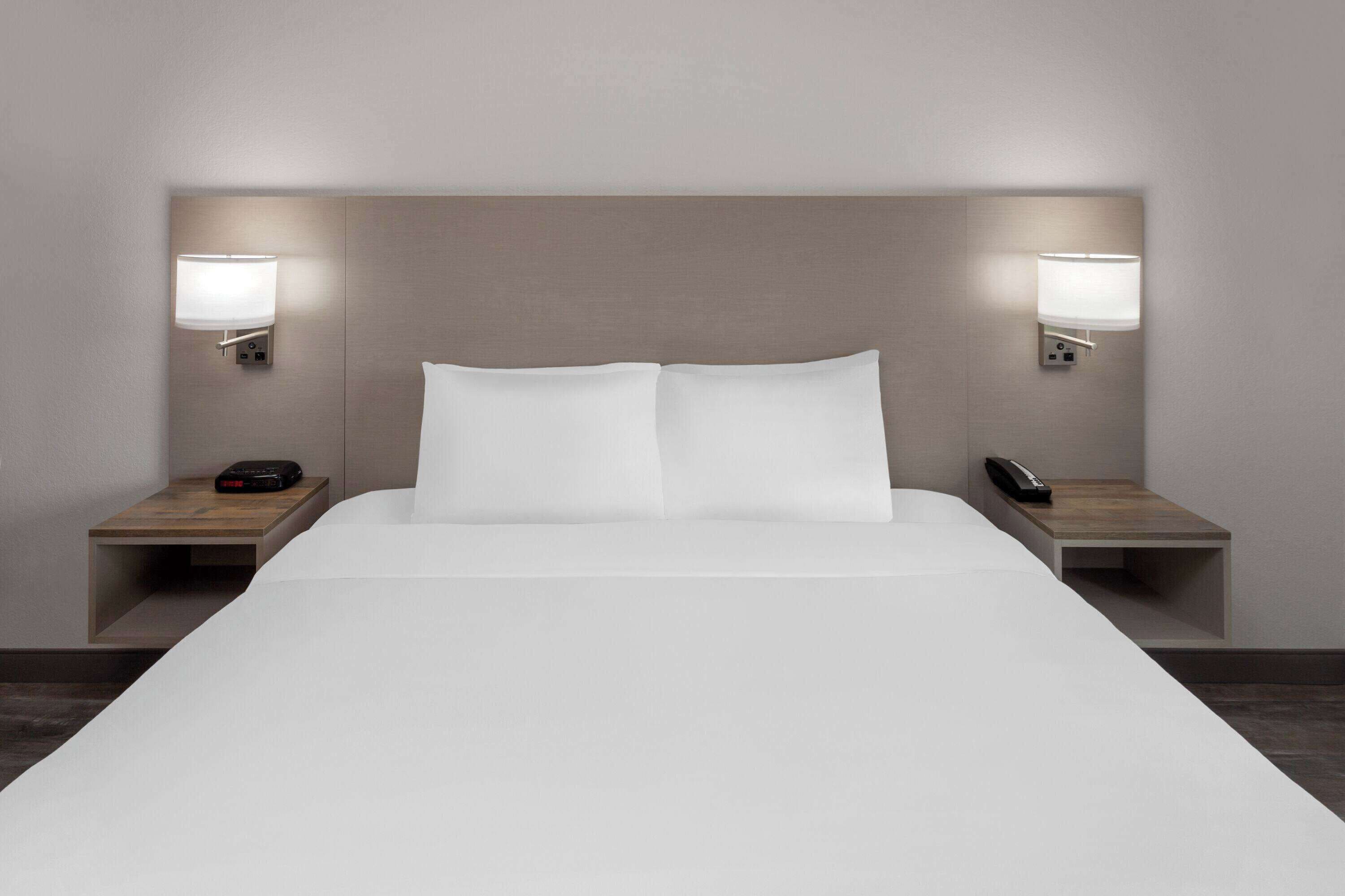 Una habitación de hotel moderna con una cama grande, dos mesitas de noche y lámparas de pared.
