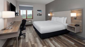 Ein modernes Hotelzimmer mit einem großen Bett, einem Schreibtisch mit Stuhl, einem Flachbildfernseher, einer Kaffeemaschine und einem Fenster mit Blick ins Freie.