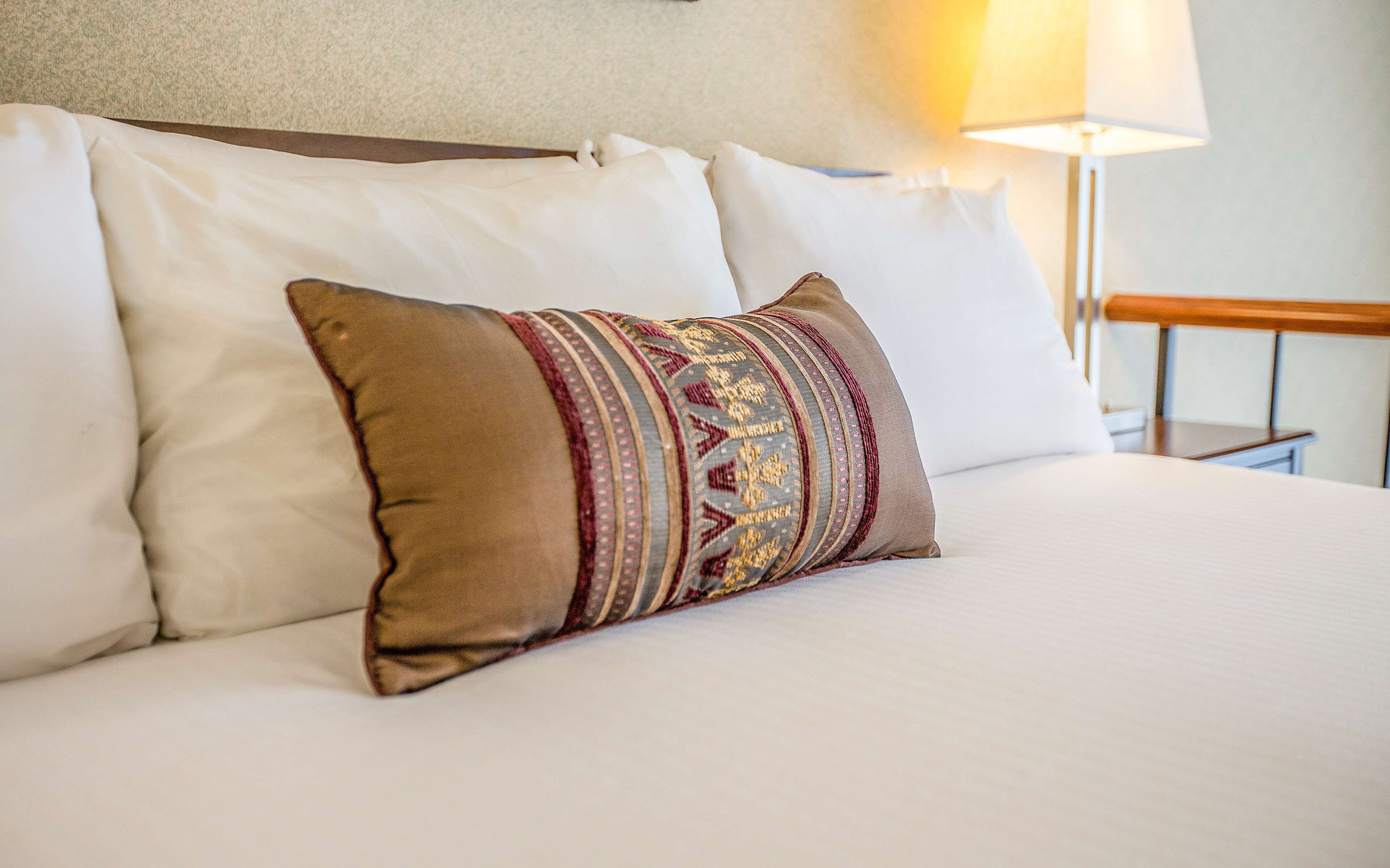 A bed with white bedding and a decorative pillow with a patterned design.