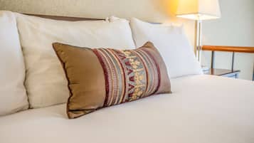 A bed with white bedding and a decorative pillow with a patterned design.