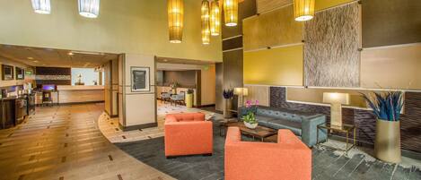 A hotel lobby with a reception desk, seating area, and a large wall with a textured design.