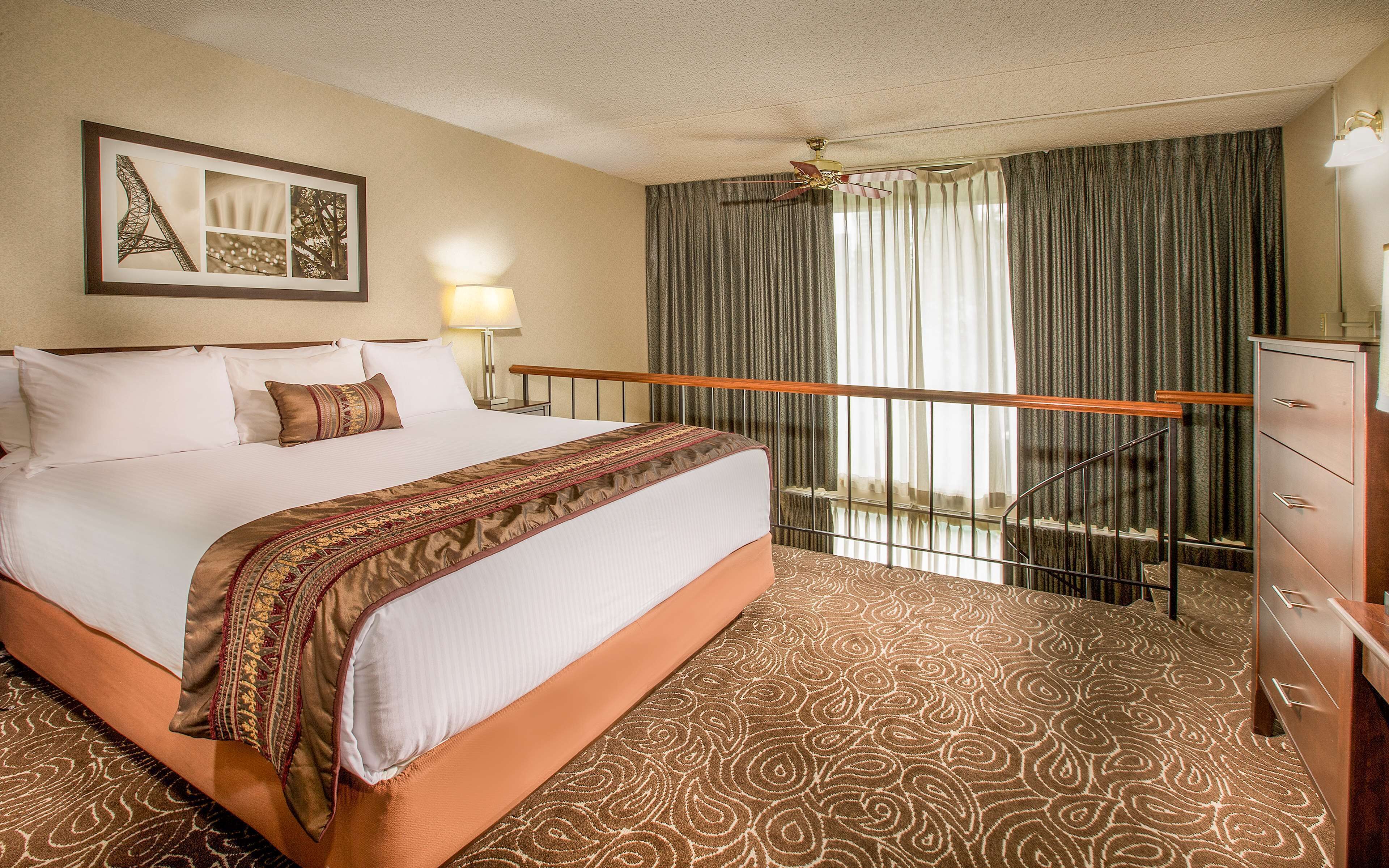 A hotel room with a large bed, a ceiling fan, a picture of the Eiffel Tower, a desk, and a dresser.