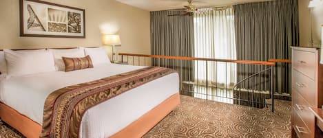 Habitación de hotel con una cama grande, ventilador de techo, un cuadro de la Torre Eiffel, un escritorio y un aparador.