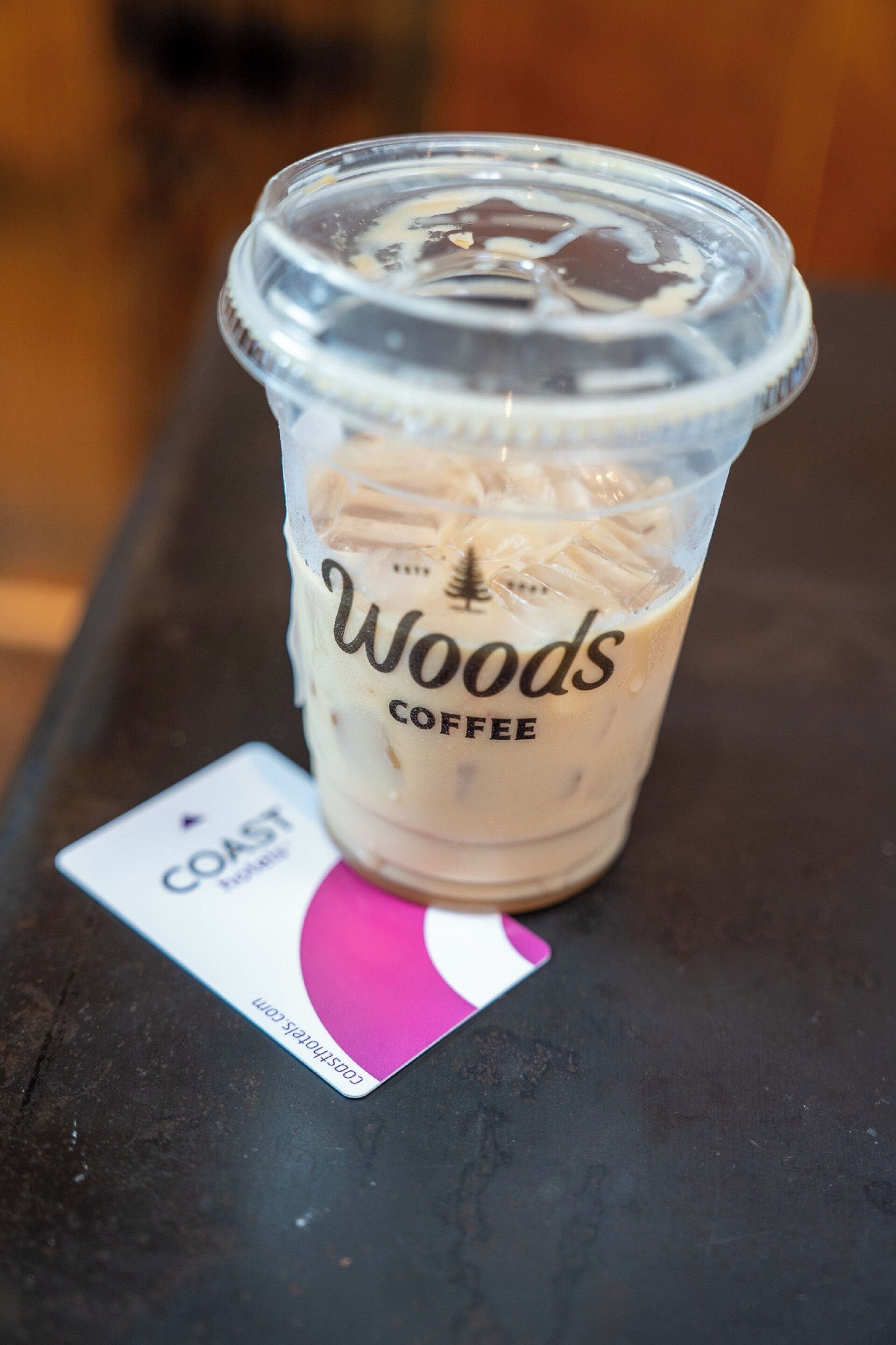 Un vaso de plástico transparente con una etiqueta que dice "Woods Coffee" y un posavasos debajo.