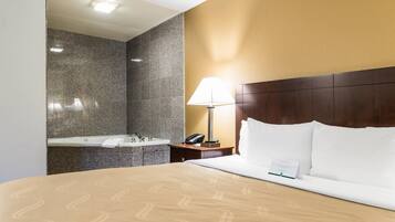 Quarto de hotel com cama, mesa de cabeceira, abajur, telefone e banheiro com pia e espelho.