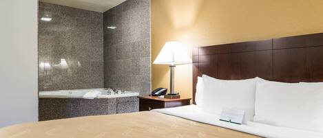 Quarto de hotel com cama, mesa de cabeceira, abajur, telefone e banheiro com pia e espelho.