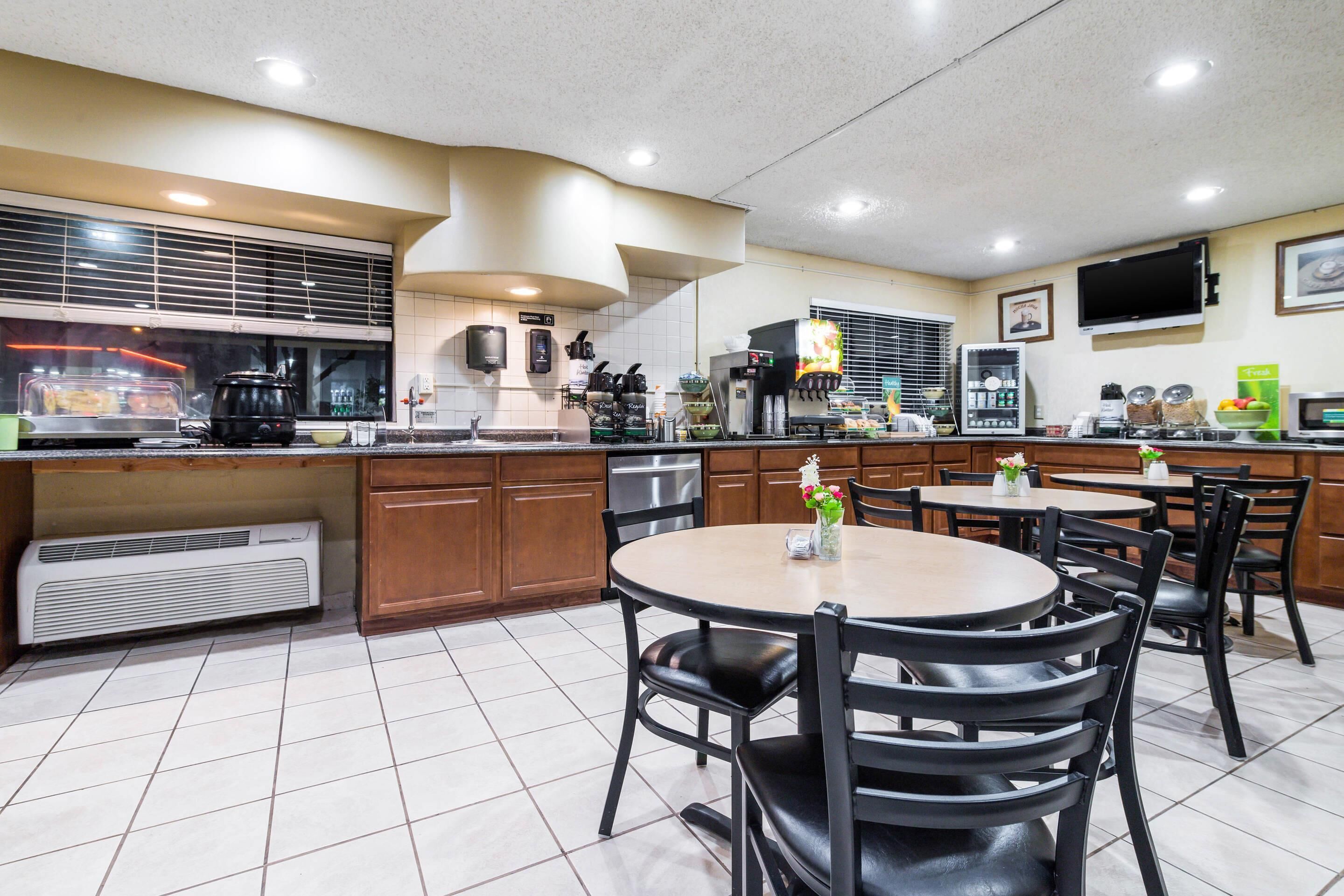 A restaurant with a kitchen area, dining tables, chairs, and a TV mounted on the wall.