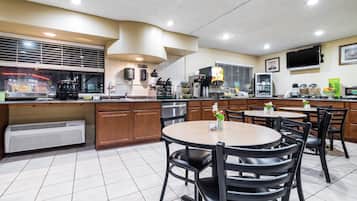 A restaurant with a kitchen area, dining tables, chairs, and a TV mounted on the wall.