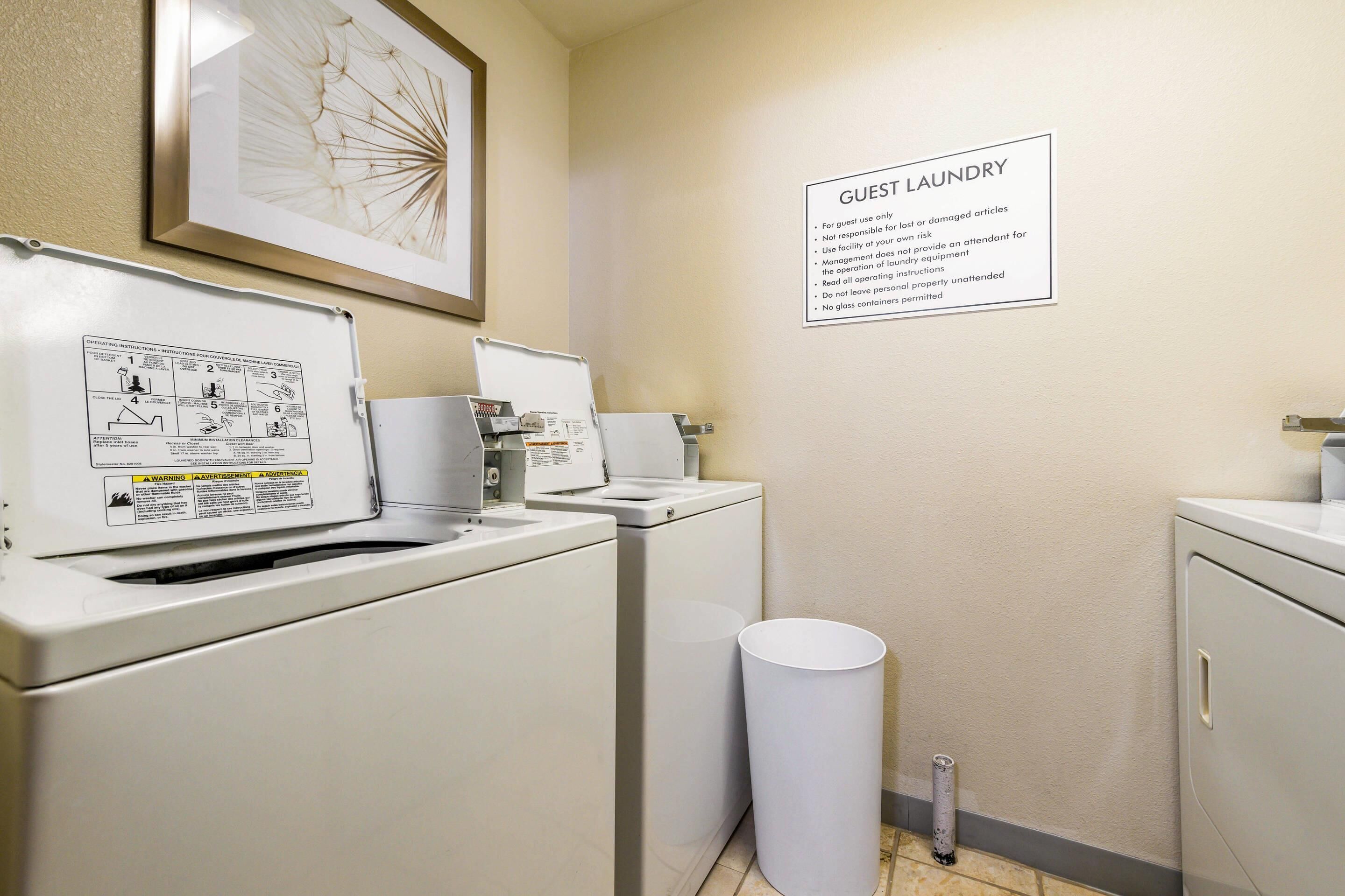 A laundry area with a sign indicating it's for guest use only, a white trash bin, and a framed artwork on the wall.