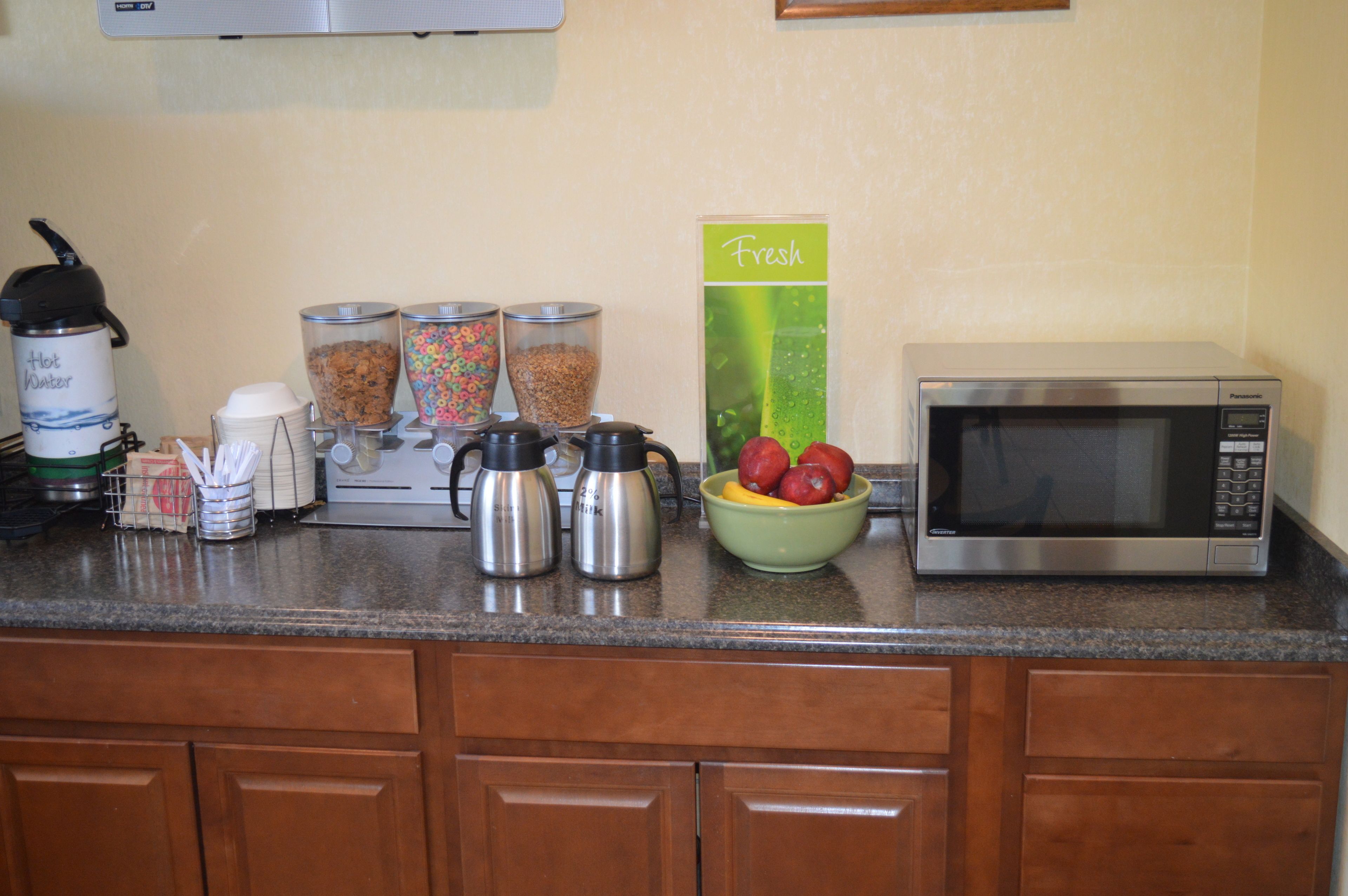 A kitchen counter with a microwave, coffee makers, and a bowl of fruit.
