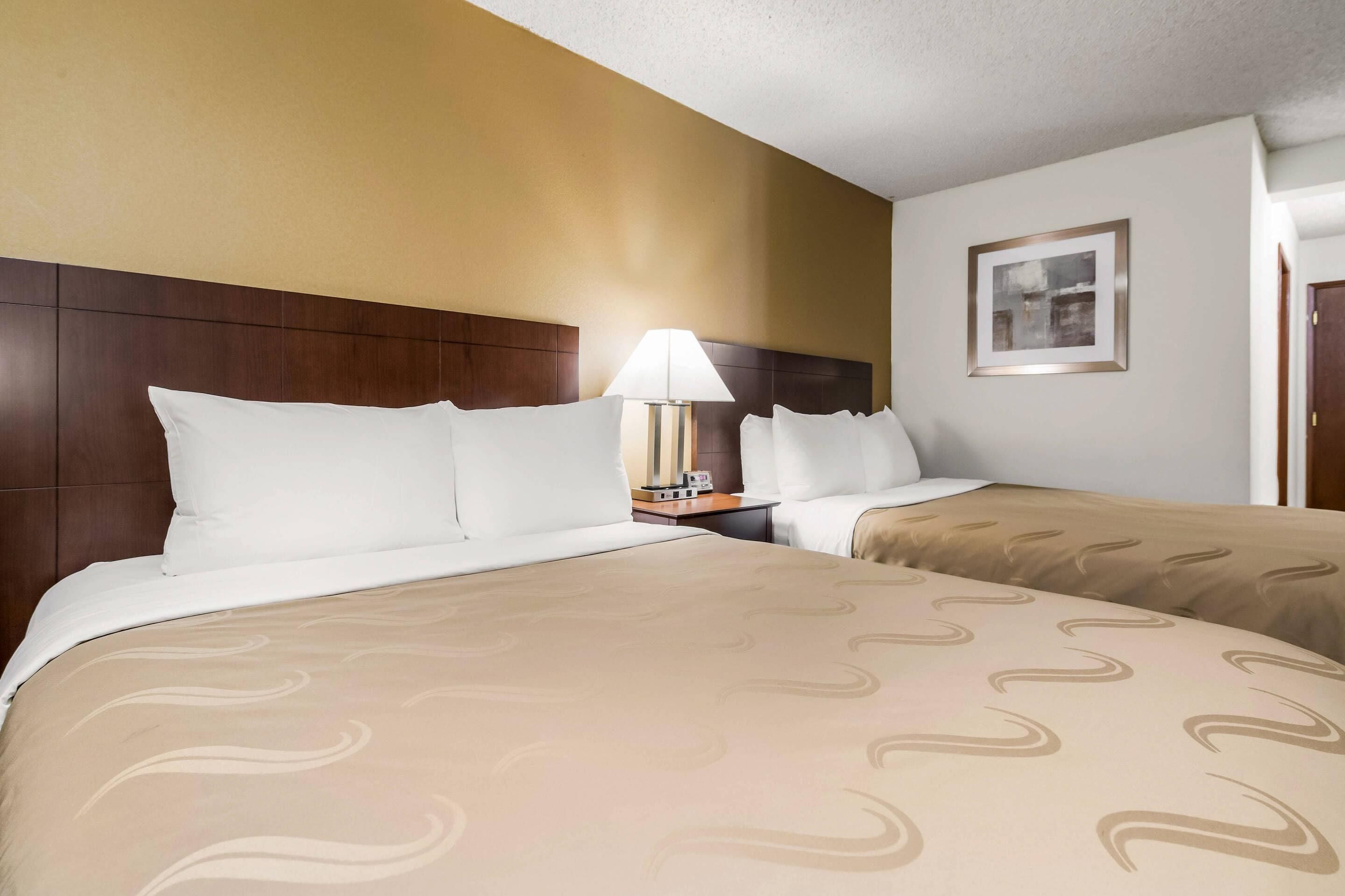 A hotel room with two beds, a nightstand with a lamp, and a framed picture on the wall.