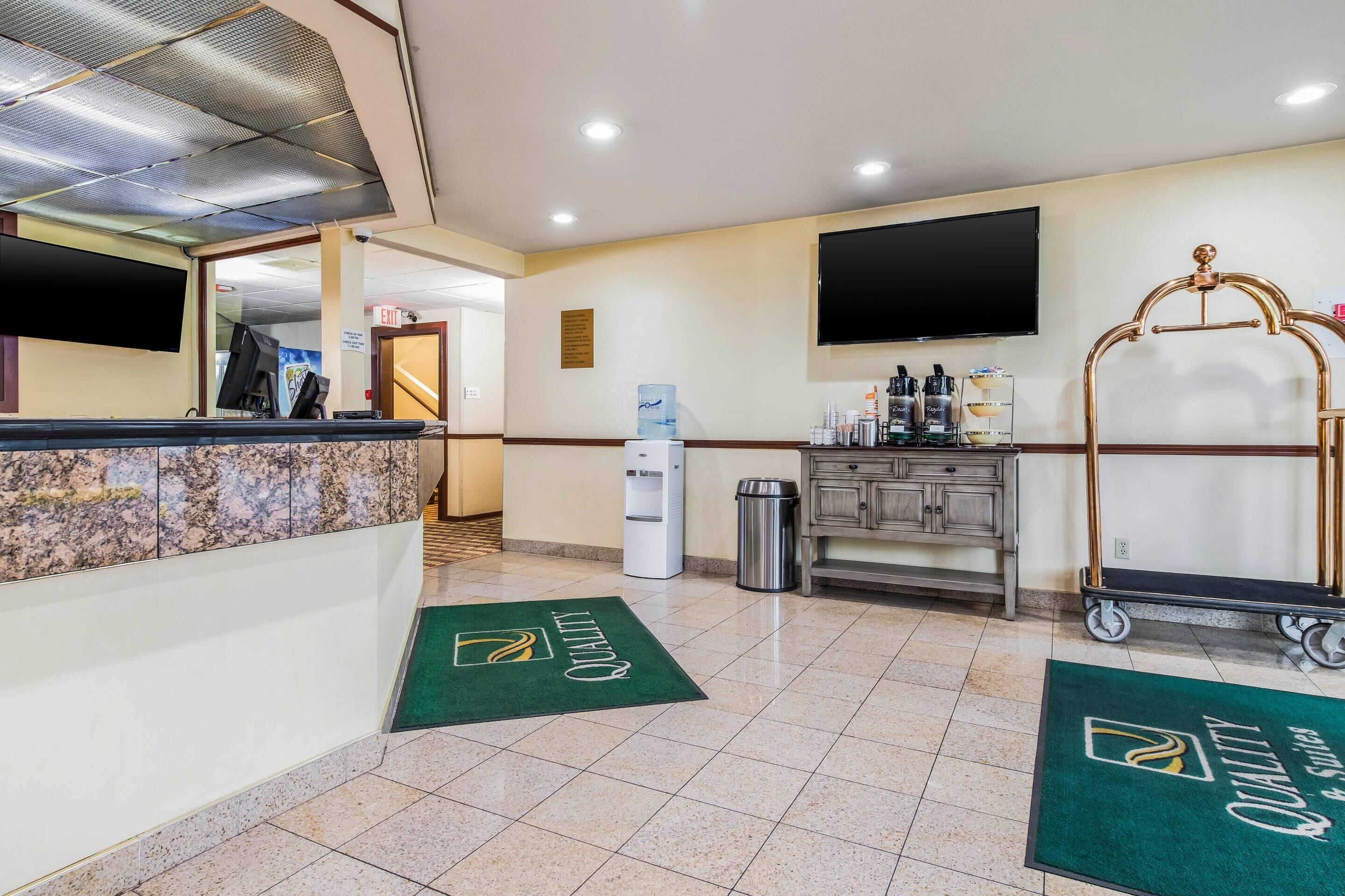 A hotel reception area with a marble counter, a water dispenser, a trash bin, a television mounted on the wall, and a cart with a golden headrest.