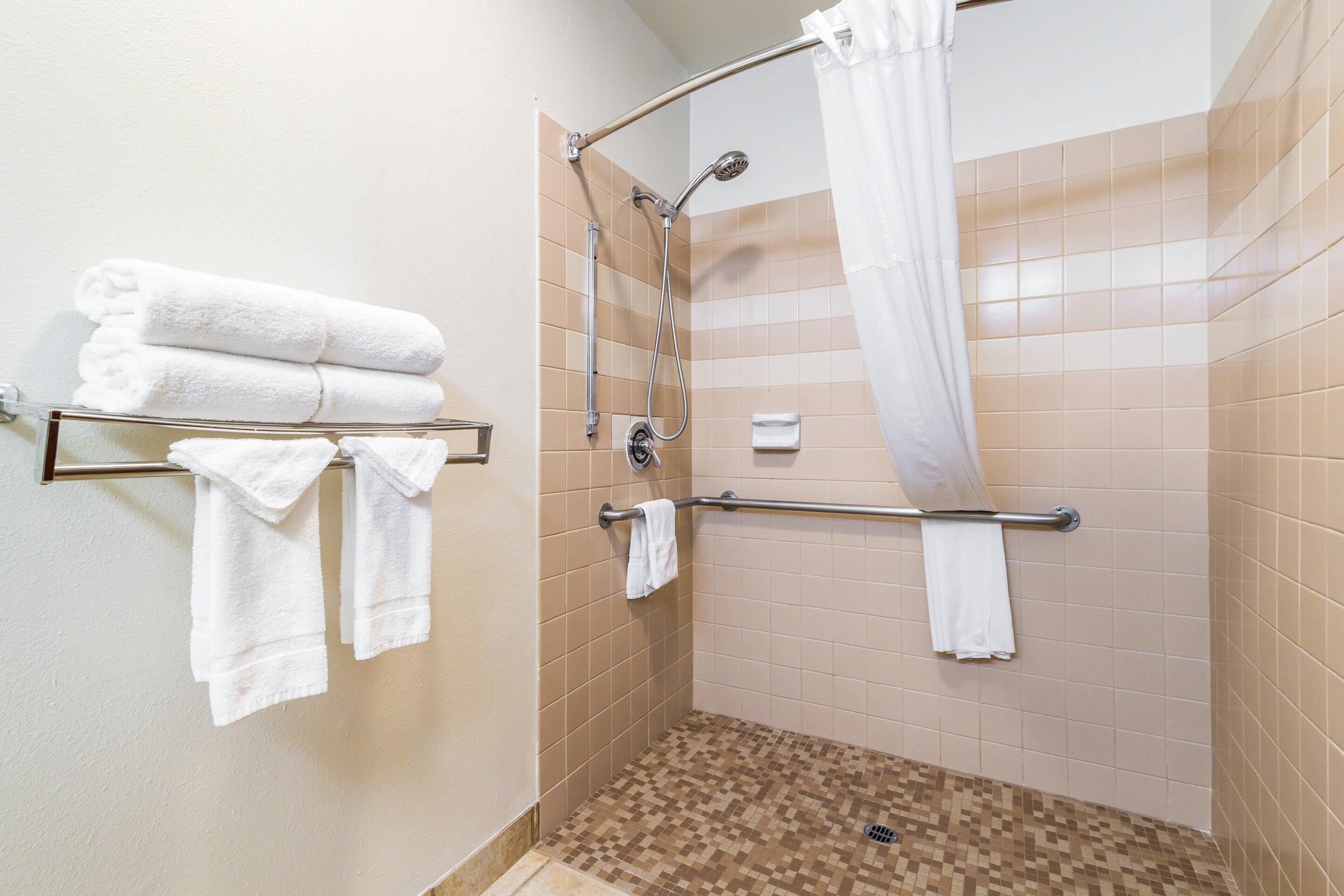 A shower area with beige tiles, a glass shower enclosure, and a metal towel rack with folded towels.