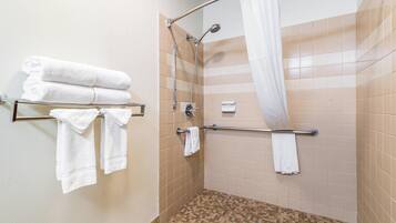 A shower area with beige tiles, a glass shower enclosure, and a metal towel rack with folded towels.