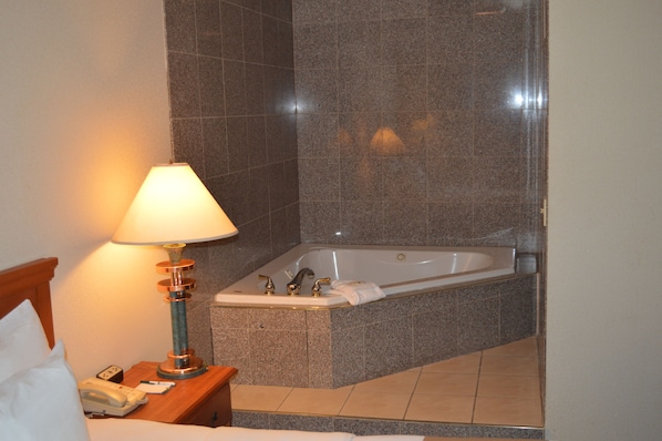 A bathroom with a bathtub, a bedside table with a lamp, and a telephone.
