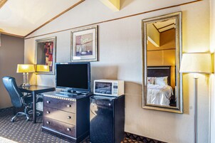 Habitación de hotel con escritorio, televisión, microondas, cómoda, silla y un espejo grande.