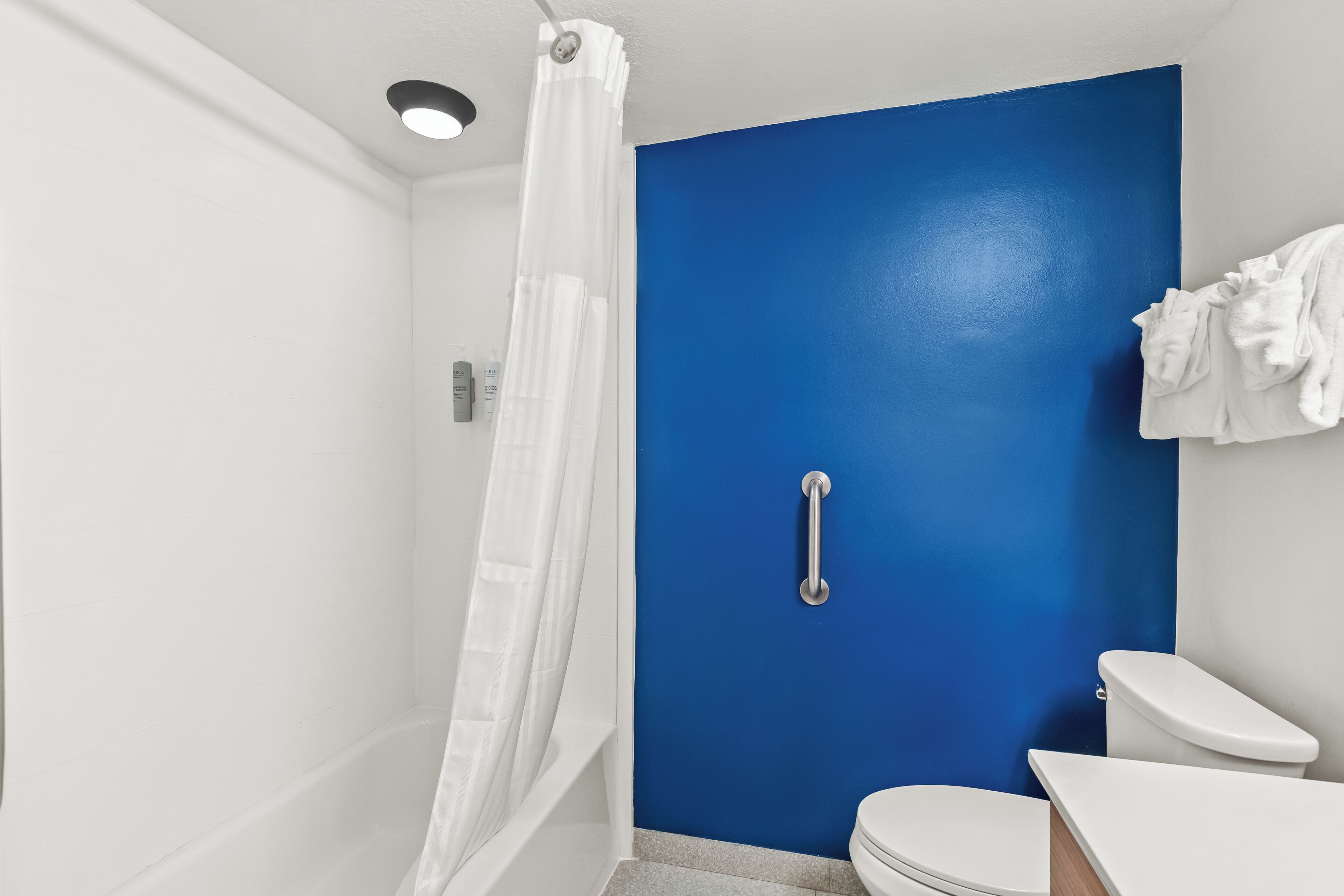 Un baño con una pared azul decorativa, un inodoro blanco, ducha con cortina blanca y una barandilla.