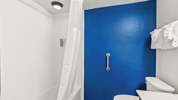 Un baño con una pared azul decorativa, un inodoro blanco, ducha con cortina blanca y una barandilla.