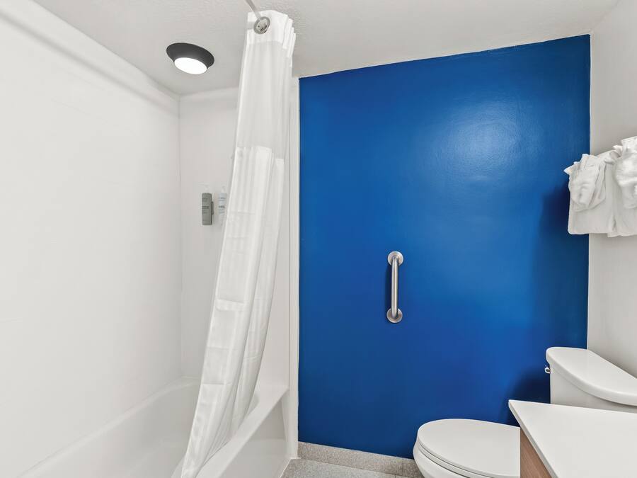 Un baño con una pared azul decorativa, un inodoro blanco, ducha con cortina blanca y una barandilla.