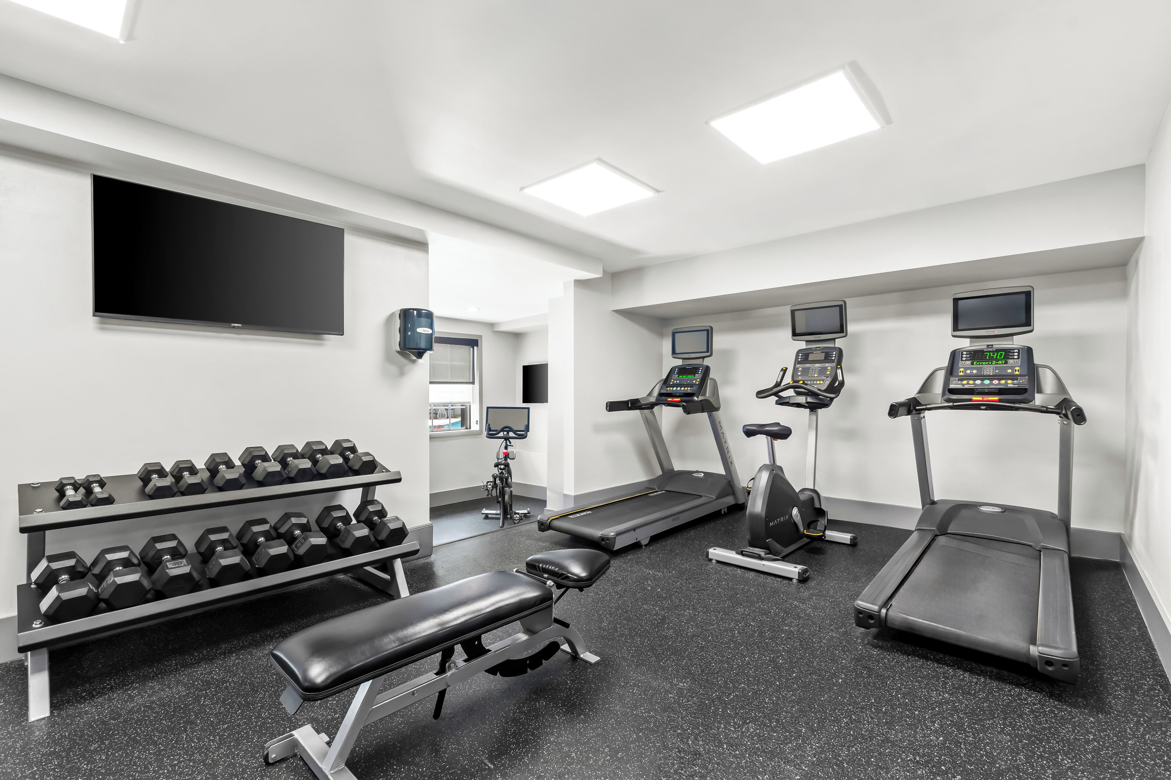 Un gimnasio con cintas de correr, elíptica, banco y mancuernas.