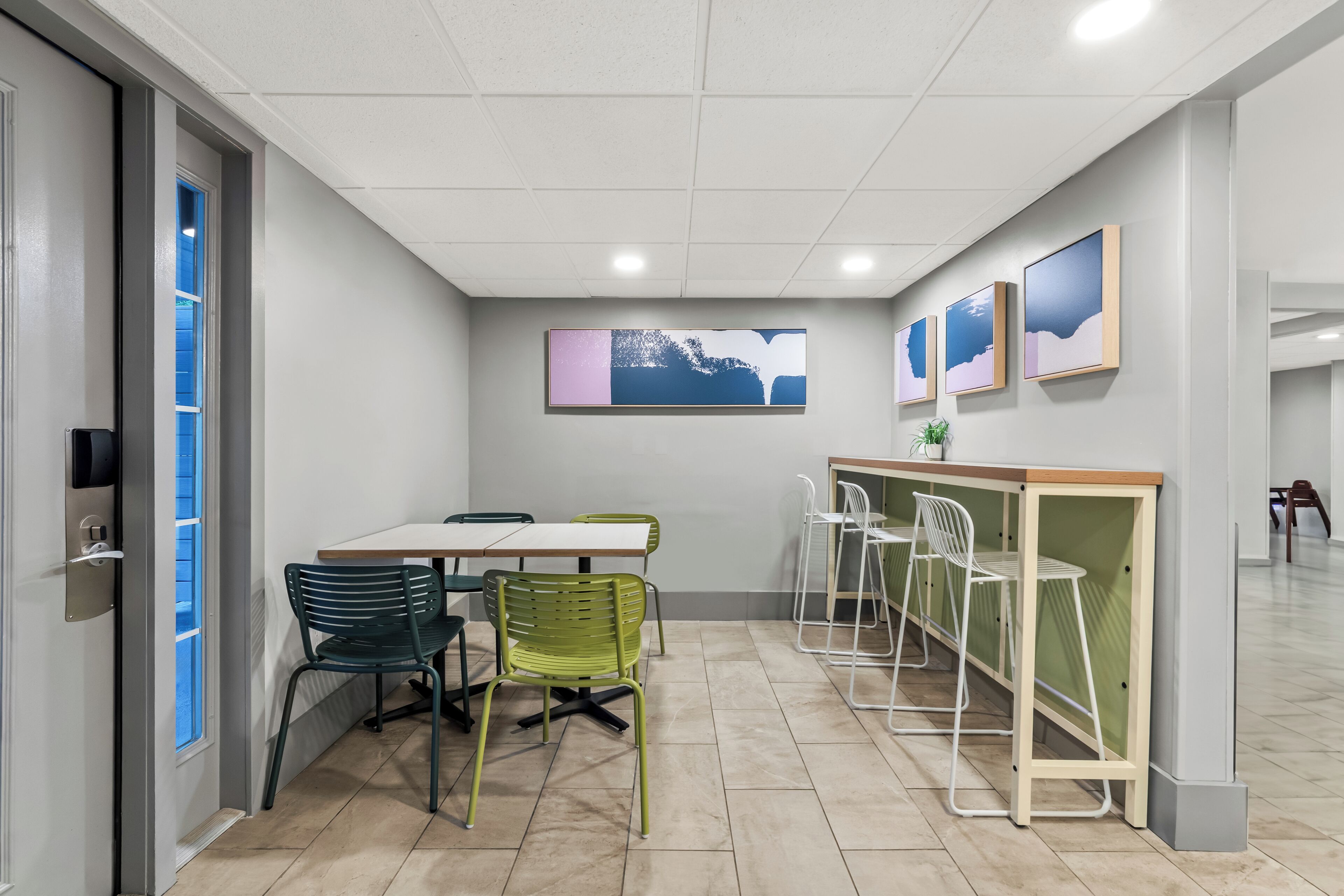 A conference room with a white table, green chairs, a white bar area, and framed artwork on the wall.