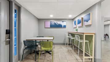 A conference room with a white table, green chairs, a white bar area, and framed artwork on the wall.