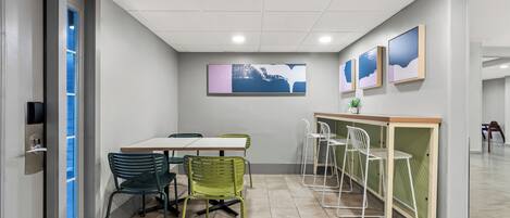 Une salle de conférence avec une table blanche, des chaises vertes, un comptoir blanc et des œuvres d’art encadrées accrochées au mur.