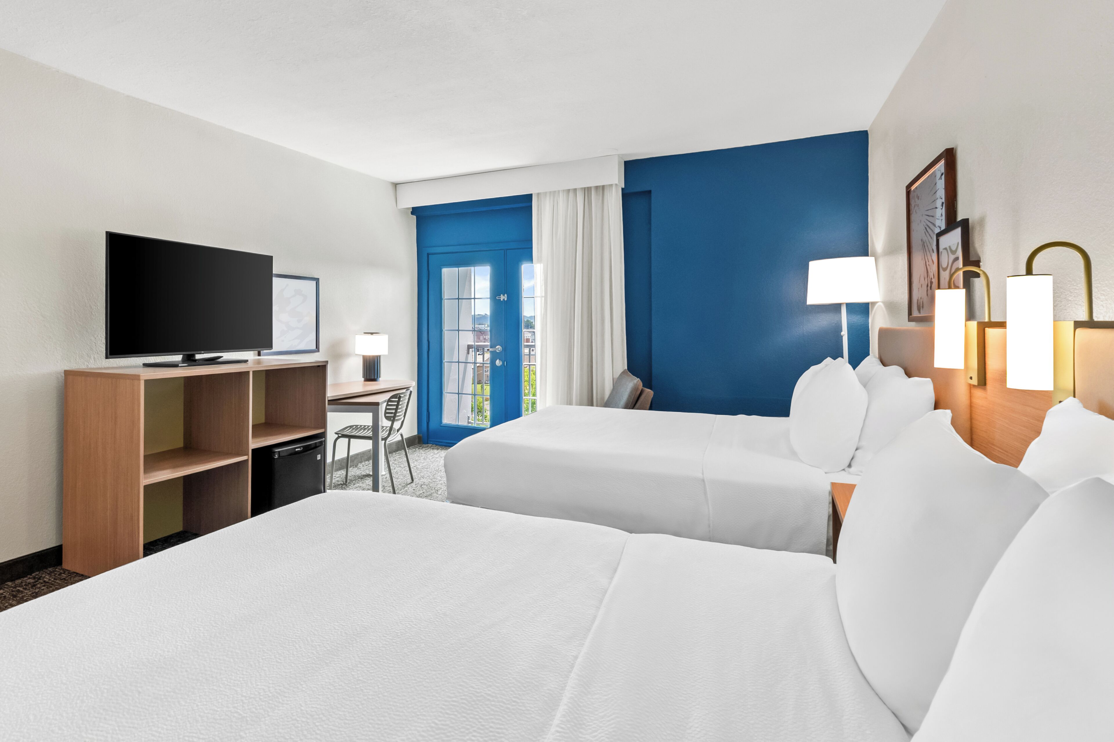 Habitación de hotel con dos camas, un escritorio, un televisor y una ventana con cortinas.