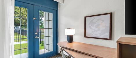 Una habitación con una puerta azul, un escritorio con lámpara, una silla y un cuadro en la pared.