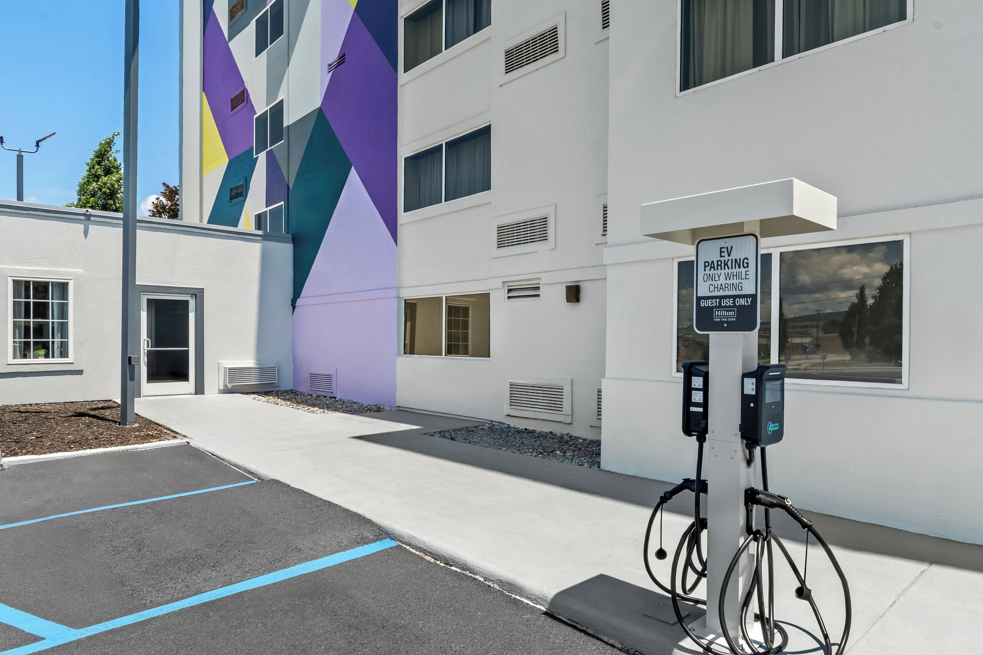 An EV charging station in front of a modern building with a colorful geometric facade.