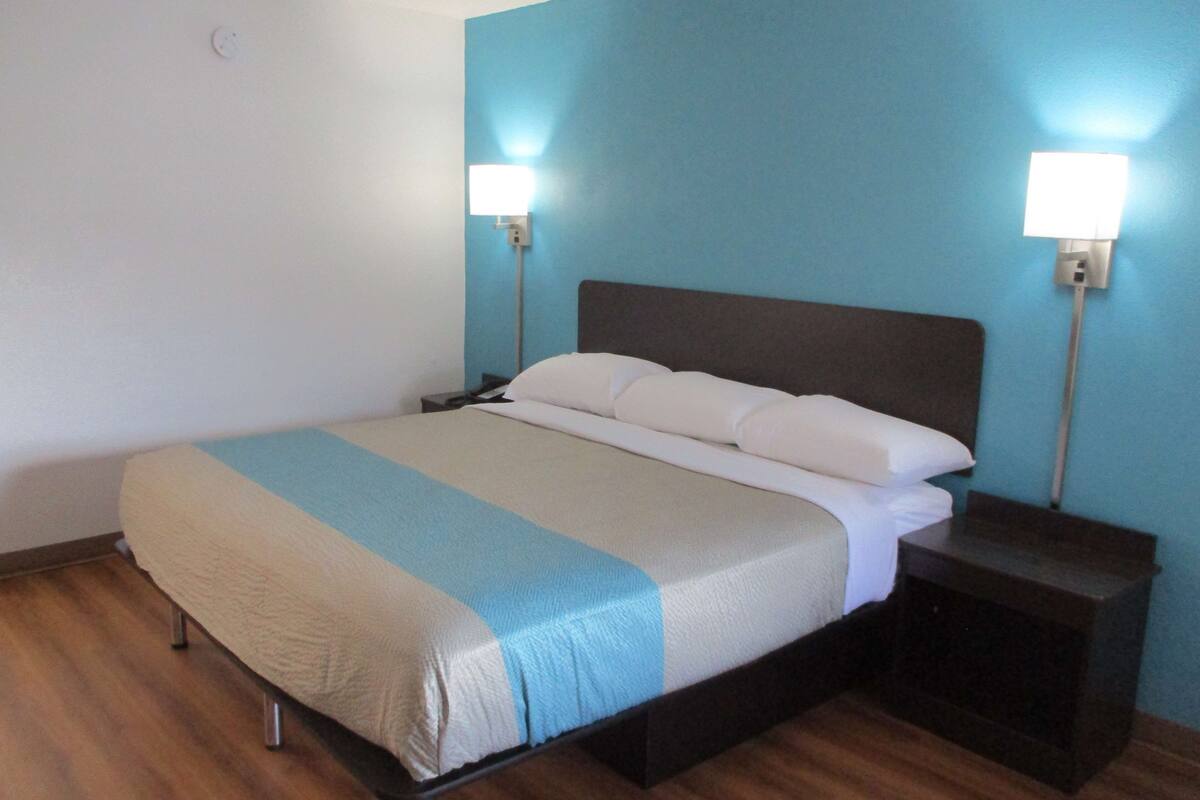 A hotel room with a bed, two bedside tables, and wall-mounted lights.