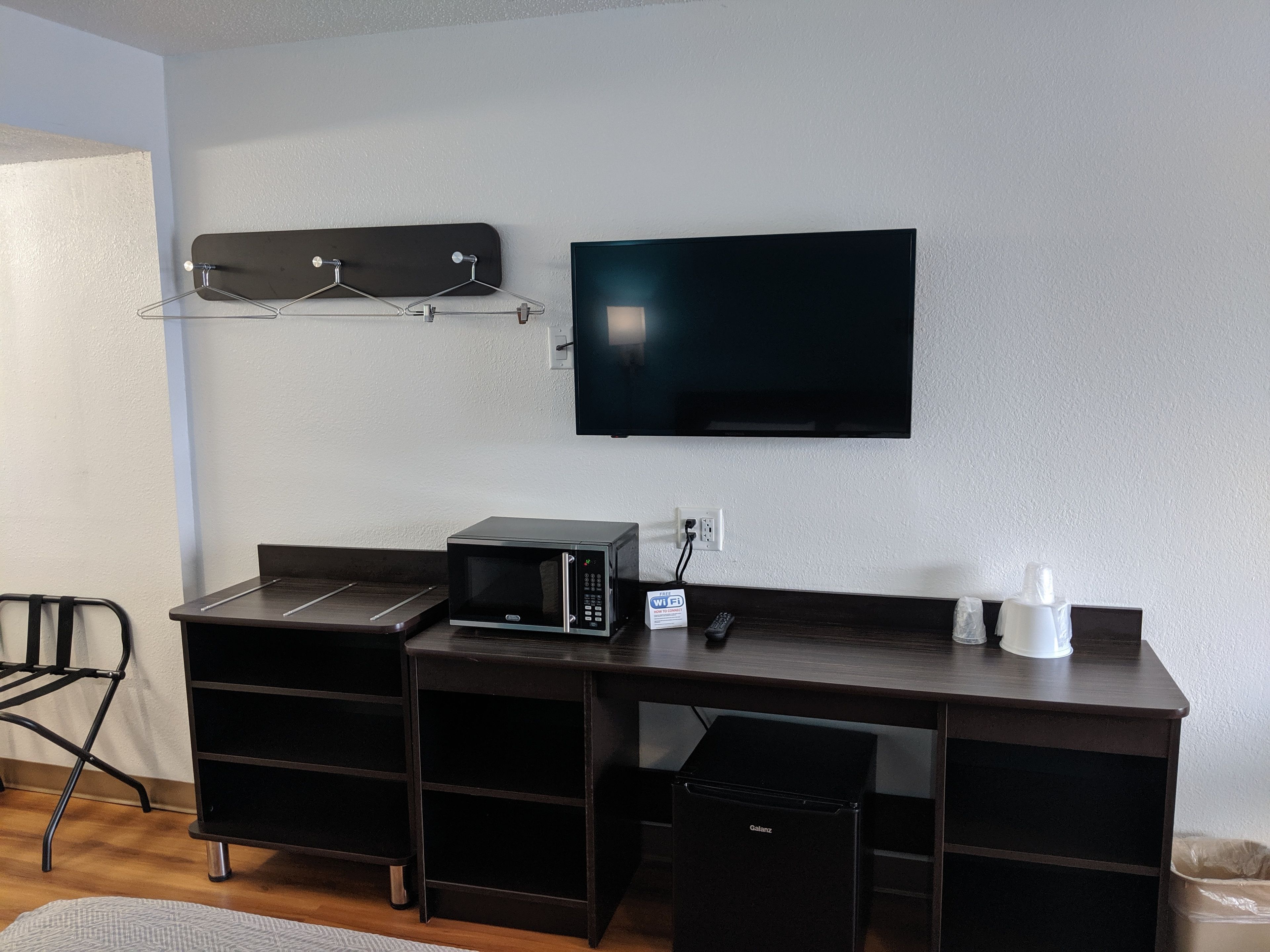 Une chambre moderne dotée d’un bureau en bois foncé, d’un téléviseur à écran plat fixé au mur, d’un four à micro-ondes et d’un petit réfrigérateur.
