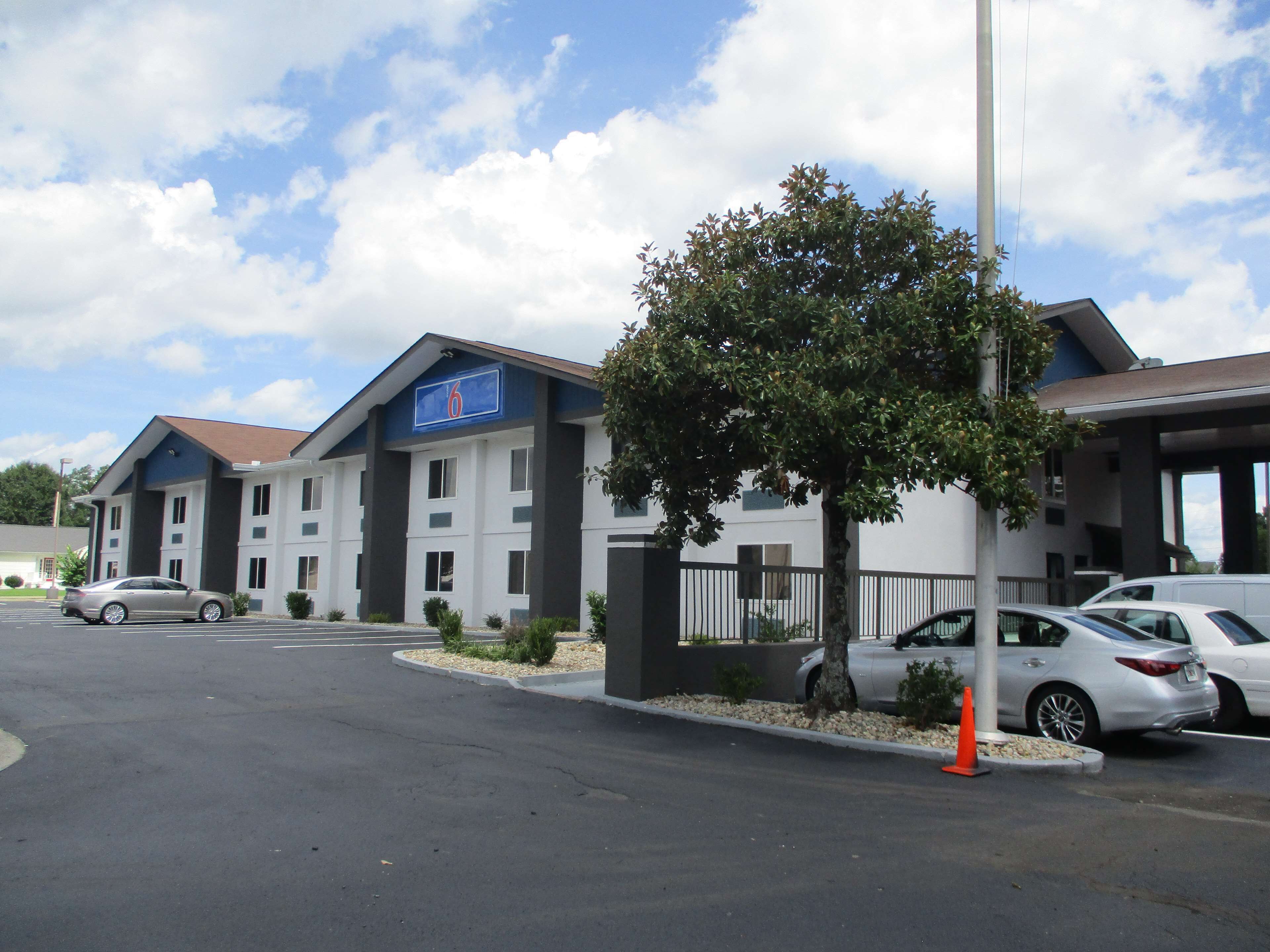 Un hôtel avec une enseigne portant le chiffre « 6 », un parking et un arbre au premier plan.