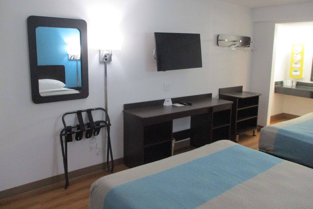 A hotel room with a bed, a desk, a chair, a TV, and a mirror.