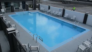 A rectangular pool with a metal ladder and white lounge chairs around it.