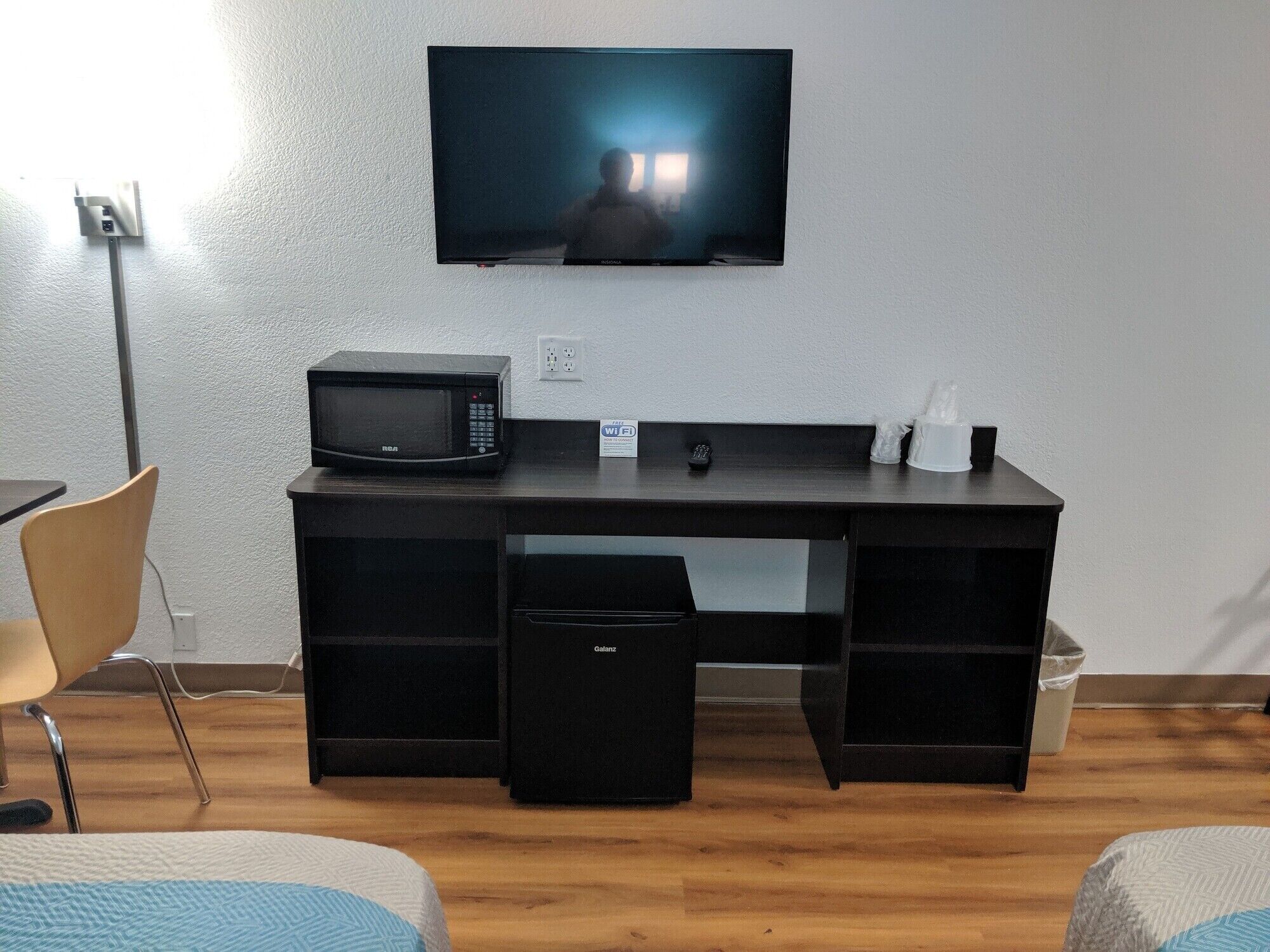 A hotel room with a desk, a microwave, a TV, a chair, and a small trash bin.