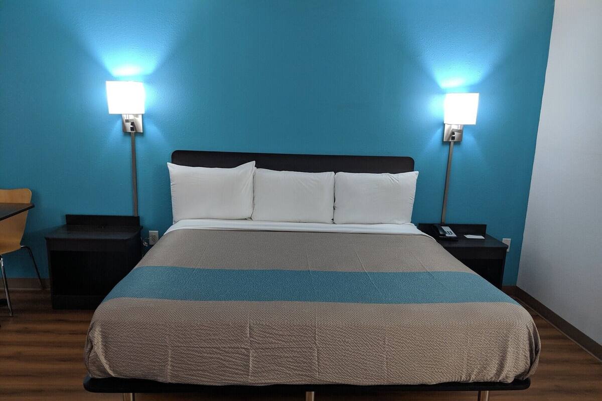 A hotel room with a bed, two bedside tables, a chair, and two wall-mounted lamps.
