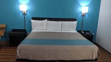 Une chambre d’hôtel comprenant un lit, deux tables de chevet, une chaise et deux lampes fixées au mur.