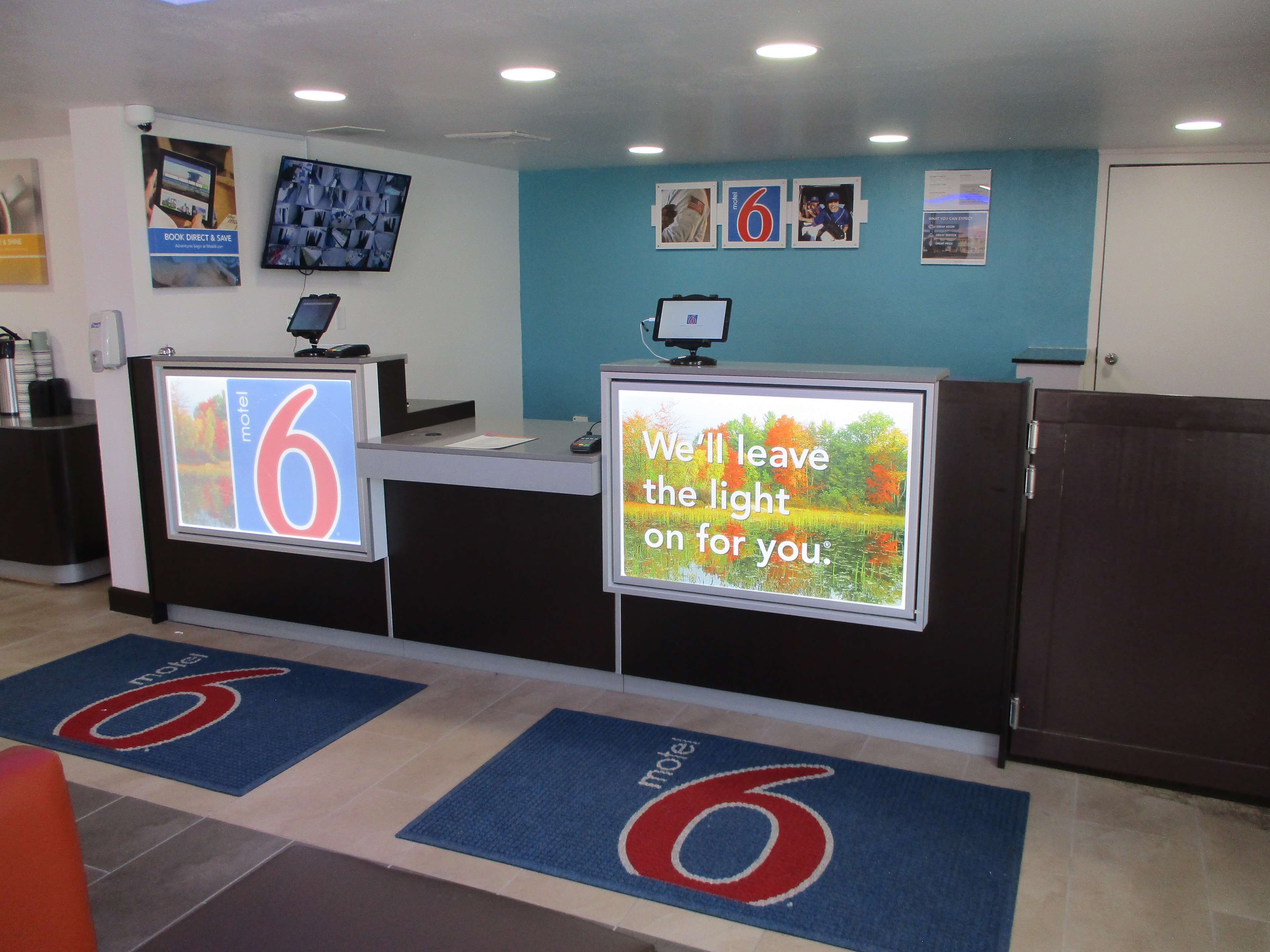 A hotel reception area with a digital display board, a desk, and a door.