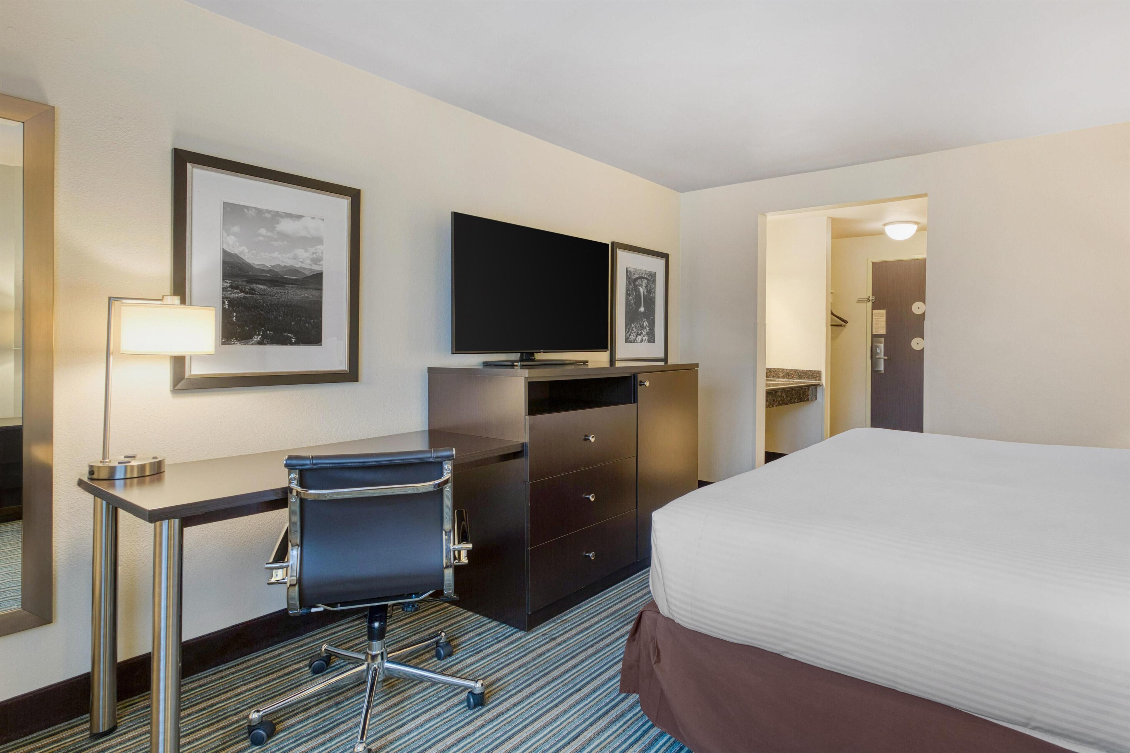 Una habitación de hotel con cama, escritorio y silla, televisor y cómoda.
